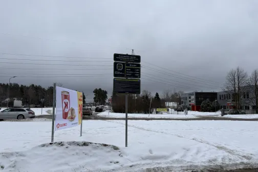 Sniegots laukums ar ceļa zīmēm, pelēkas debesis.