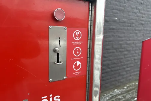 Sarkans maksājumu automāts ar monētu spraugu autostāvvietas mazgātavā.