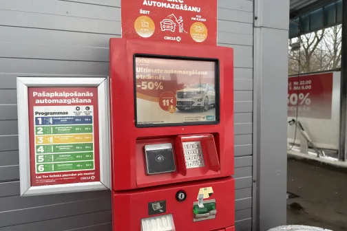 Automazgātuves maksājumu automāts ar ekrānu un cenu sarakstu.