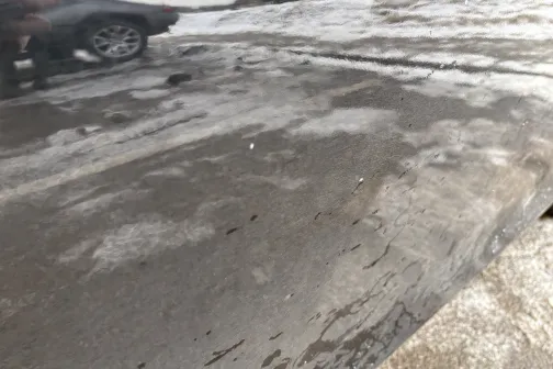 Automa&scaron;īnas spoguļattēls uz slapjas virsmas ar netīru ceļu un automa&scaron;īnu fonā.