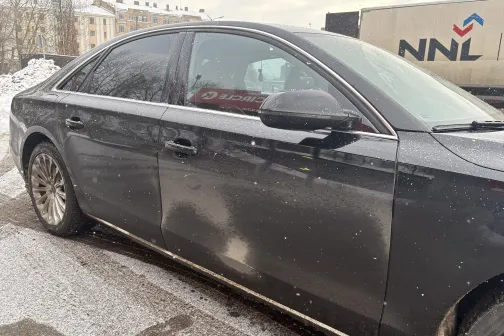 Melns sedans ar netīriem sāniem stāv uz sniegota ceļa.