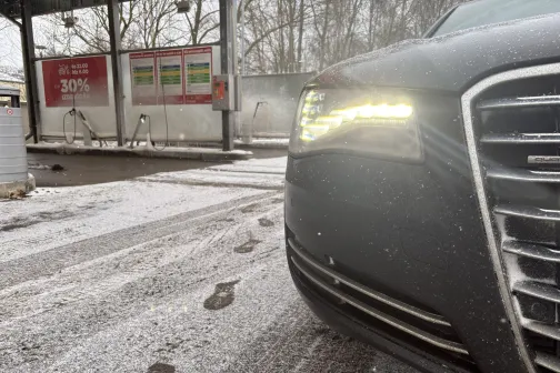 Melna automa&scaron;īna ar ieslēgtām priek&scaron;ējām lukturiem sniegotā mazgātavā.