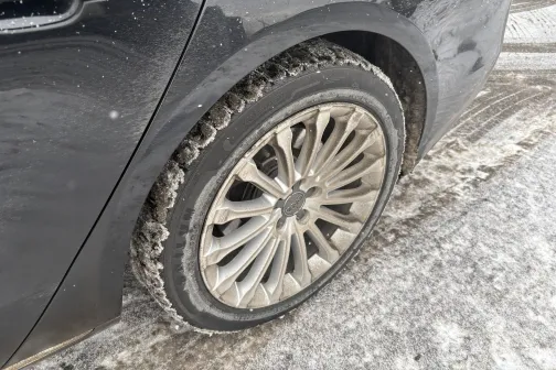 Melnas automa&scaron;īnas aizmugurējais ritenis uz netīra ceļa ziemā.