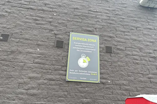 Zīmola plakāts pie pelēkas ķieģeļu sienas.