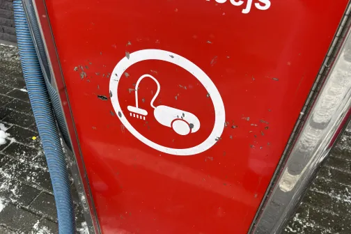 Sarkans panelis ar balta putekļsūcēja simbolu un zilu cauruli.