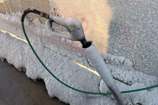 Putu pārklāta sasalusi auto mazgā&scaron;anas pistole pie sienas.