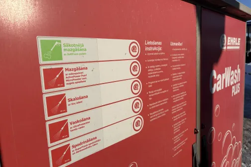 Sarkana ma&scaron;īnas mazgātavas instrukciju siena saulainā dienā.