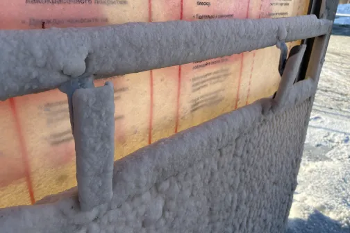 Sniega un ledus pārklāta automazgātuves siena saulē.