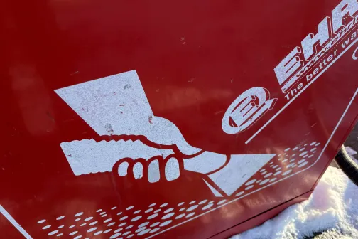 Balts grafisks logotips uz sarkana fona, attēlojot roku ar putekļusūcēju.