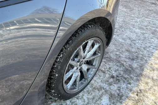 Pelēcīga automa&scaron;īna uz sniegota ceļa, sānskata ritenis spīd saulē.