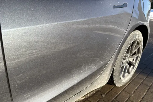 Netīrs sudraba auto sāns uz bruģa, fokusēts uz aizmugurējo riteņu daļu.