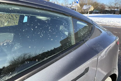 Auto sānskats ar putekļiem uz loga saulainā ziemas dienā.