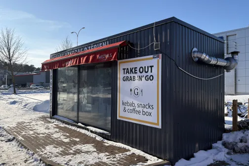 Mazā, tum&scaron;a ēka saulainā ziemas dienā ar uzrakstu "Take Out".