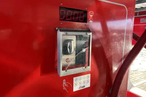 Sarkanās krāsas automazgātavas maksājumu terminālis ar digitālo ekrānu.