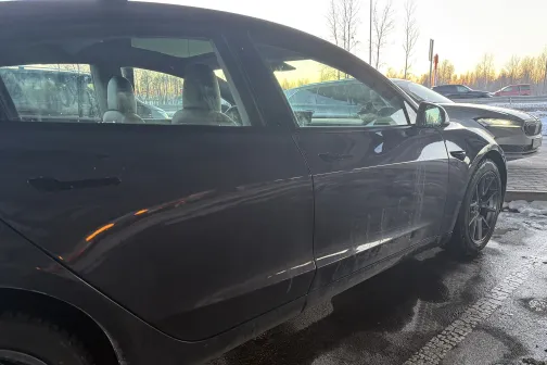 Melns auto ar slapjiem sāniem stāvvietā pie auto mazgātavas.