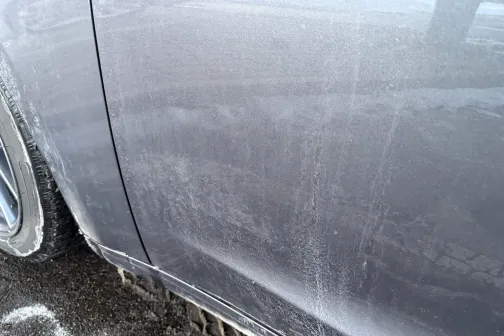 Netīrs pelēka auto sāns ar smiltīm un putekļiem.