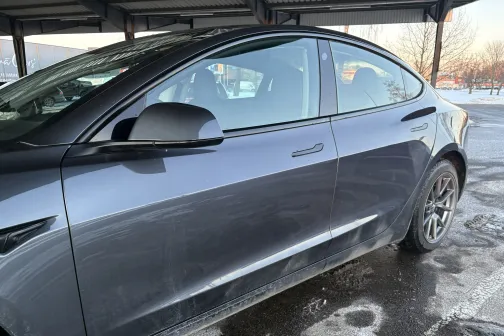 Metāliski pelēka automa&scaron;īna ar netīrumiem apak&scaron;ējā daļā stāvlaukumā ziemā.