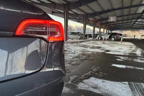 Stāvlaukumā zem nojumes ar slapju zemi stāv tum&scaron;s auto.