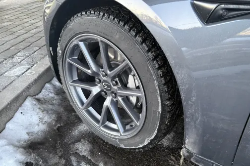 Pelēka automa&scaron;īnas riepa ar sudrabainu disku, ziemas apstākļos.