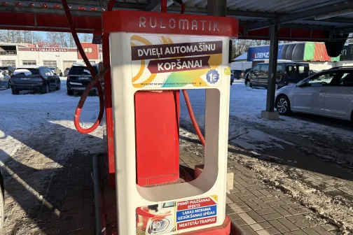 Balts un sarkans autostāvvietas mazgā&scaron;anas aparāts zem nojumes.