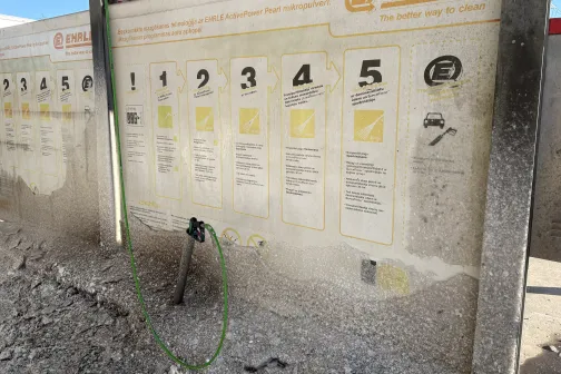 Automa&scaron;īnas mazgā&scaron;anas instrukcijas uz sienas, blakus mazgā&scaron;anas &scaron;ļūtene.