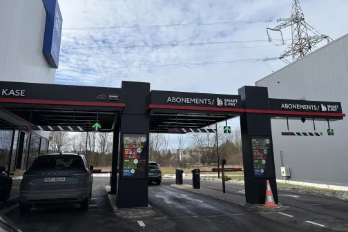 Automa&scaron;īnas piebrauc pie automazgātuves vārtiem zem zilām debesīm.