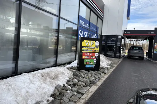 Automa&scaron;īna gaida pie automazgātuves, redzama cenu zīme.