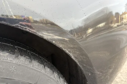 Netīrs melns auto spārns un riepa ar atspulgiem.