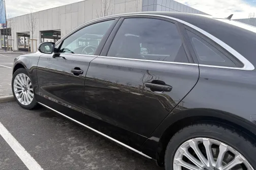 Melnā sedana sānskats autostāvvietā, skaidra debesis fonā.