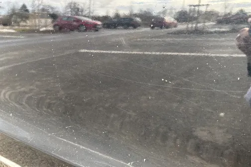 Izplūdis auto spoguļa atspulgs, redzama autostāvvieta un debesis.