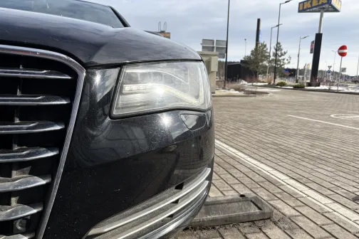 Melnas automa&scaron;īnas priek&scaron;puse uz bruģēta laukuma, redzama luktura daļa.