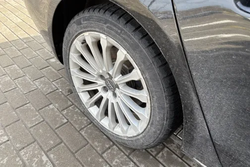 Melna automa&scaron;īna ar tīru, spīdīgu riteņu disku uz bruģa.