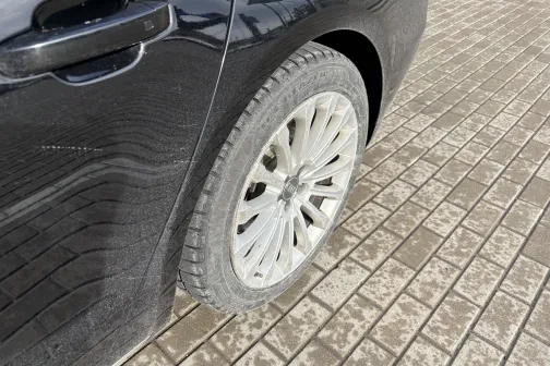 Melna automa&scaron;īna uz bruģa, fokusā aizmugurējais ritenis.