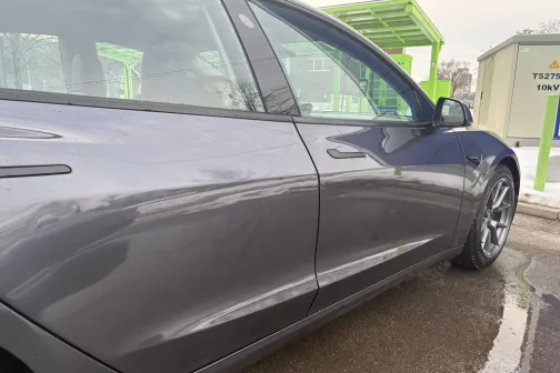 Pelēka automa&scaron;īna pie automazgātuves zaļā nojumē.