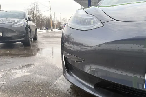 Pelēkas automa&scaron;īnas pie automazgātuves, slapj&scaron; asfalts.