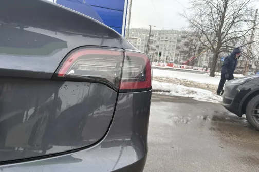 Auto aizmugures daļa ziemas pilsētvidē, redzams cilvēks tālumā.