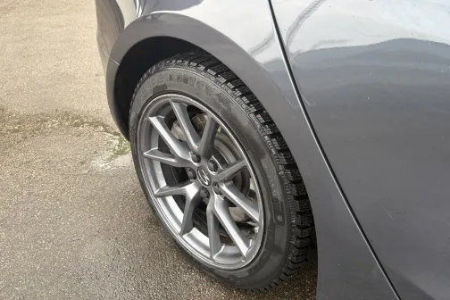 Pelēka auto aizmugurējais ritenis ar melnu riepu uz asfalta.