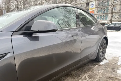 Pelēks automobilis uz netīras, sniegotas ielas malas.