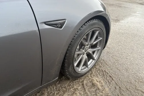 Pelēks auto uz slapjas, dubļainas ielas.