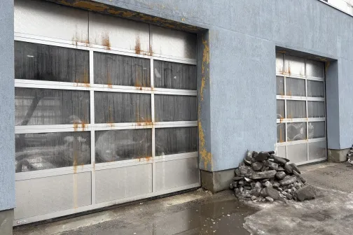 Rūsēju&scaron;i garāžas vārti, blakus akmeņu kaudze.