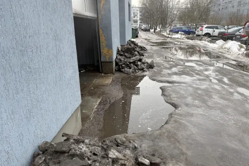 Netīrs ielas stūris ar peļķi pie ēkas, ziemas laiks.