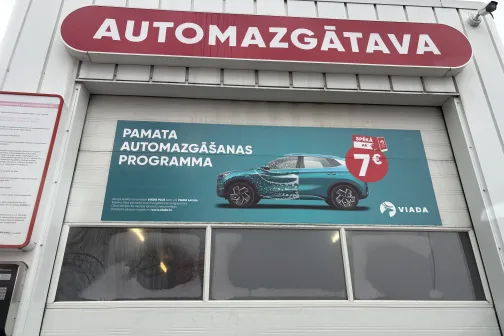 Automa&scaron;īnu mazgātavas ēka ar reklāmas plakātu uz vārtiem.