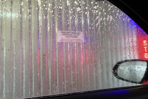 Skats caur automa&scaron;īnas logu uz auto mazgātavas sienu ar ziepju putām.