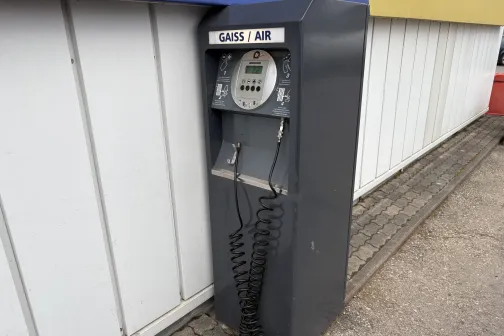 Pelēka gaisa un ūdens uzpildes iekārta pie autoservisa sienas.