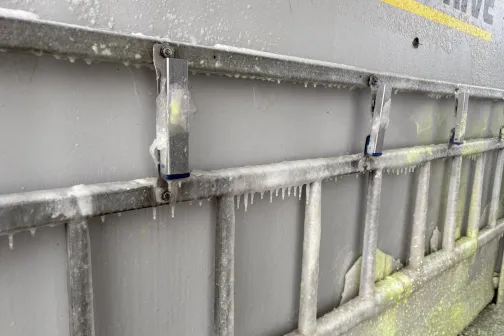 Metāla kāpnes ar ledus slāņiem uz transporta līdzekļa sāna.