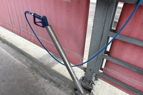 Mazgā&scaron;anas pistole ar zilu &scaron;ļūteni statīvā pie sienas Ceļavēj&scaron; automazgātavā Babītē
