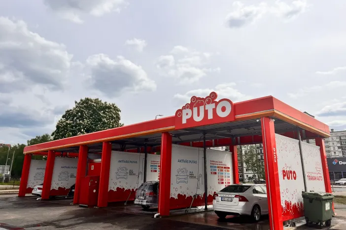 Automazgātava sarkanās un baltās krāsās zem mākoņainām debesīm.