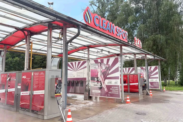 Automazgātava ar jumtu un sarkaniem akcentiem, koki fonā.