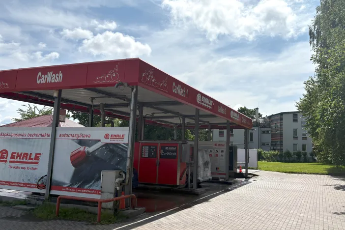 Automa&scaron;īnu mazgātava ar sarkanu nojumi un reklāmām, saulaina diena.