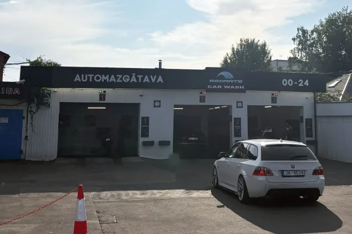 Balta automa&scaron;īna piebrauc pie automazgātavas ar trim vārtiem, saulains laiks.
